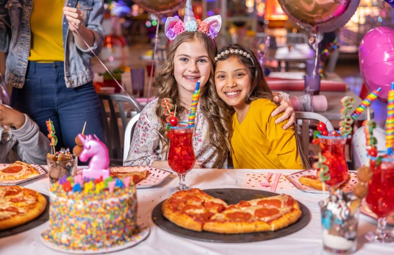 Girls celebrating birthday with cake, pizza and party drinks