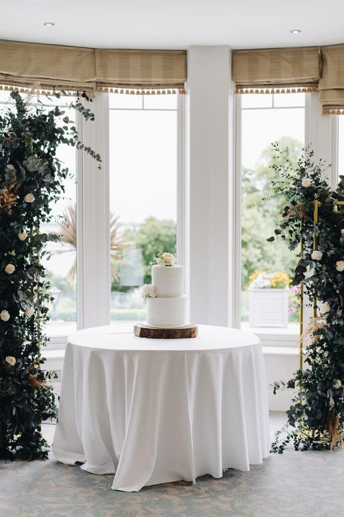 Wedding cake on table with floral arch decorations indoors