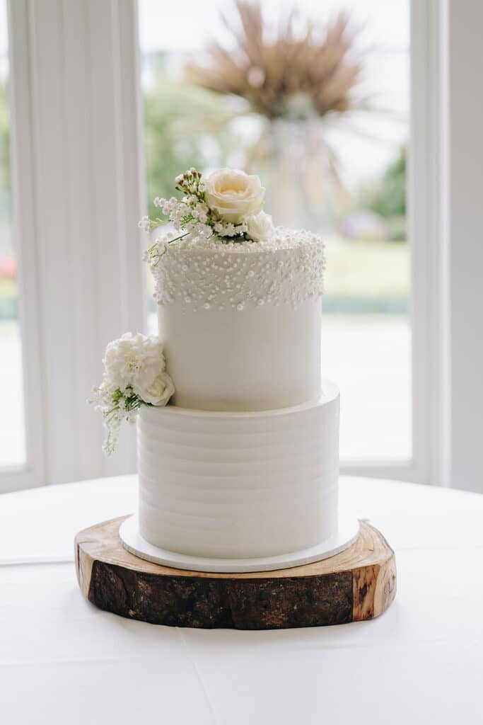Two-tier white wedding cake with pearl detail and floral topper