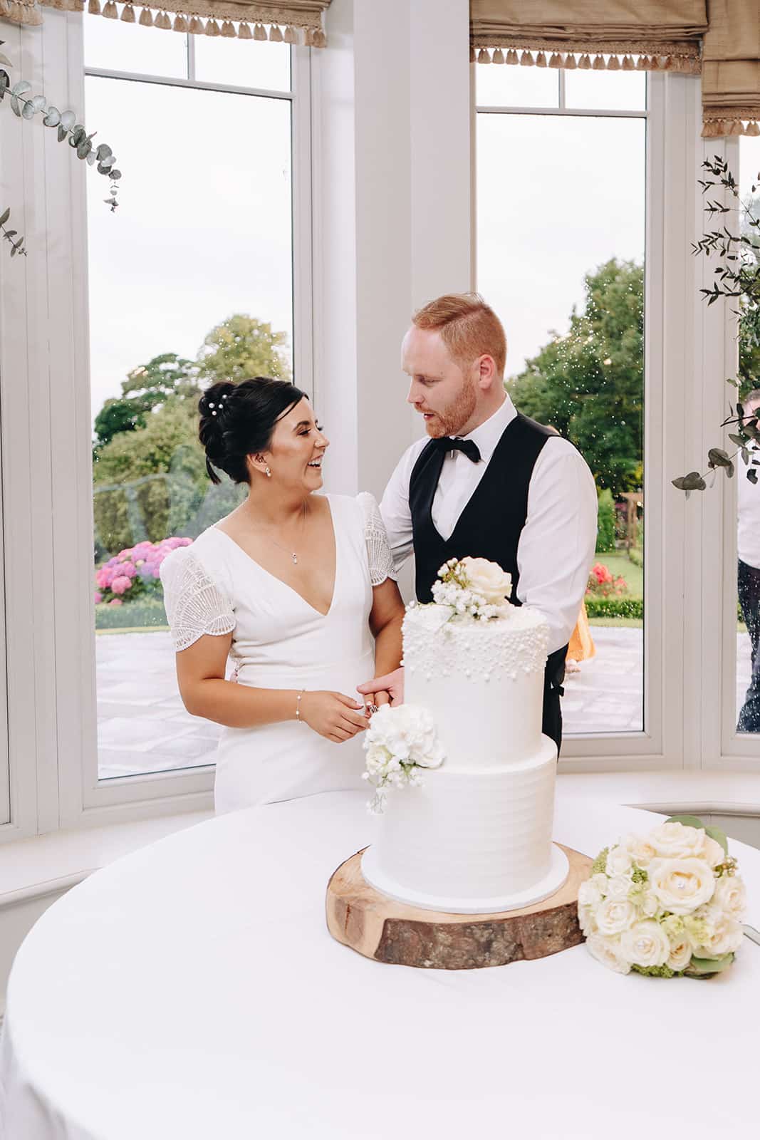 Bride and groom standing beside a white wedding cake indoors