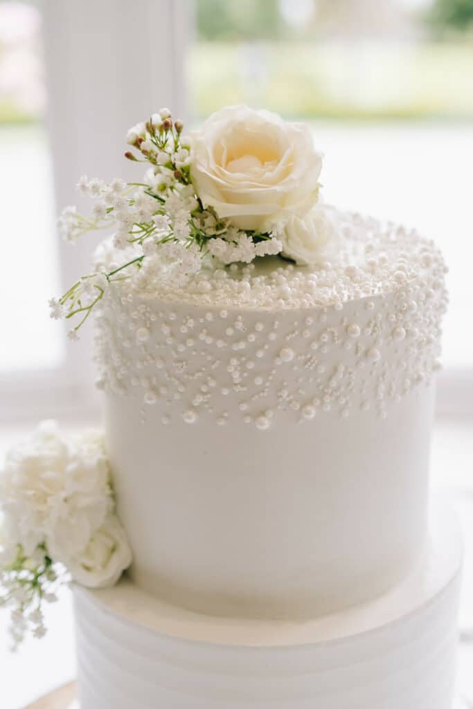 Close-up of white wedding cake with pearl detail and rose topper
