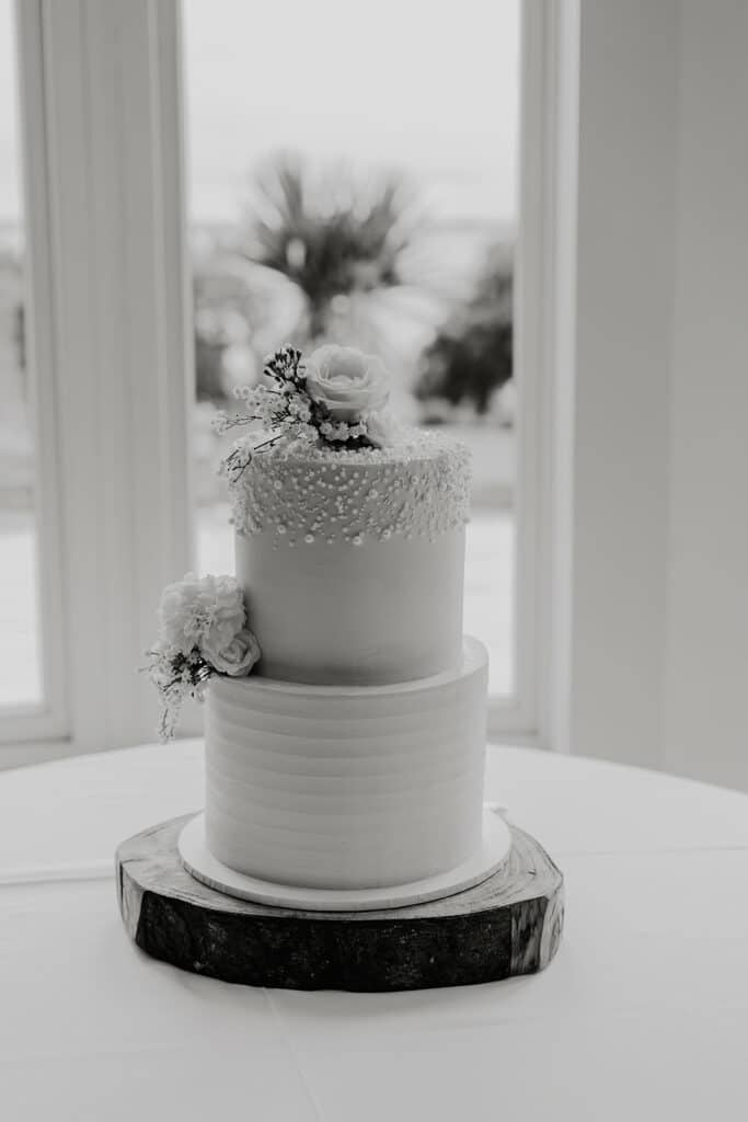 Two-tier white wedding cake with floral topper by window