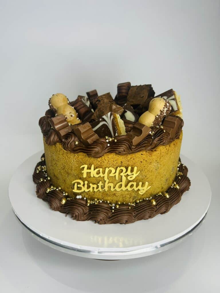 Chocolate birthday cake with sweets and “Happy Birthday” topper