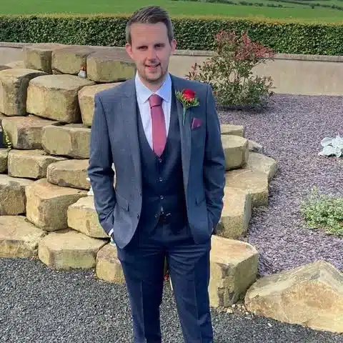 Man in suit with red tie and boutonniere outdoors