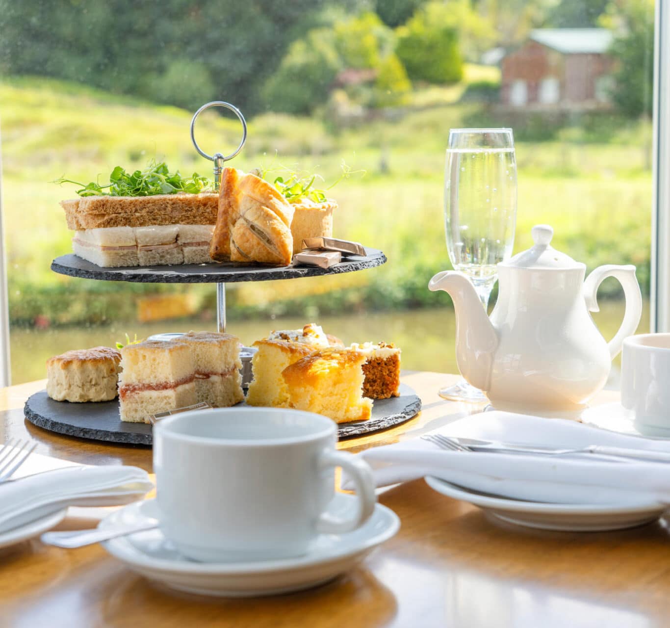 Afternoon tea set with sandwiches, cakes and teapot by window