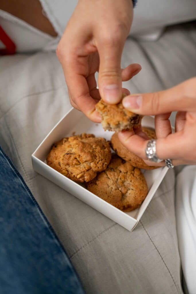 Hands breaking a cookie over a box of homemade cookies