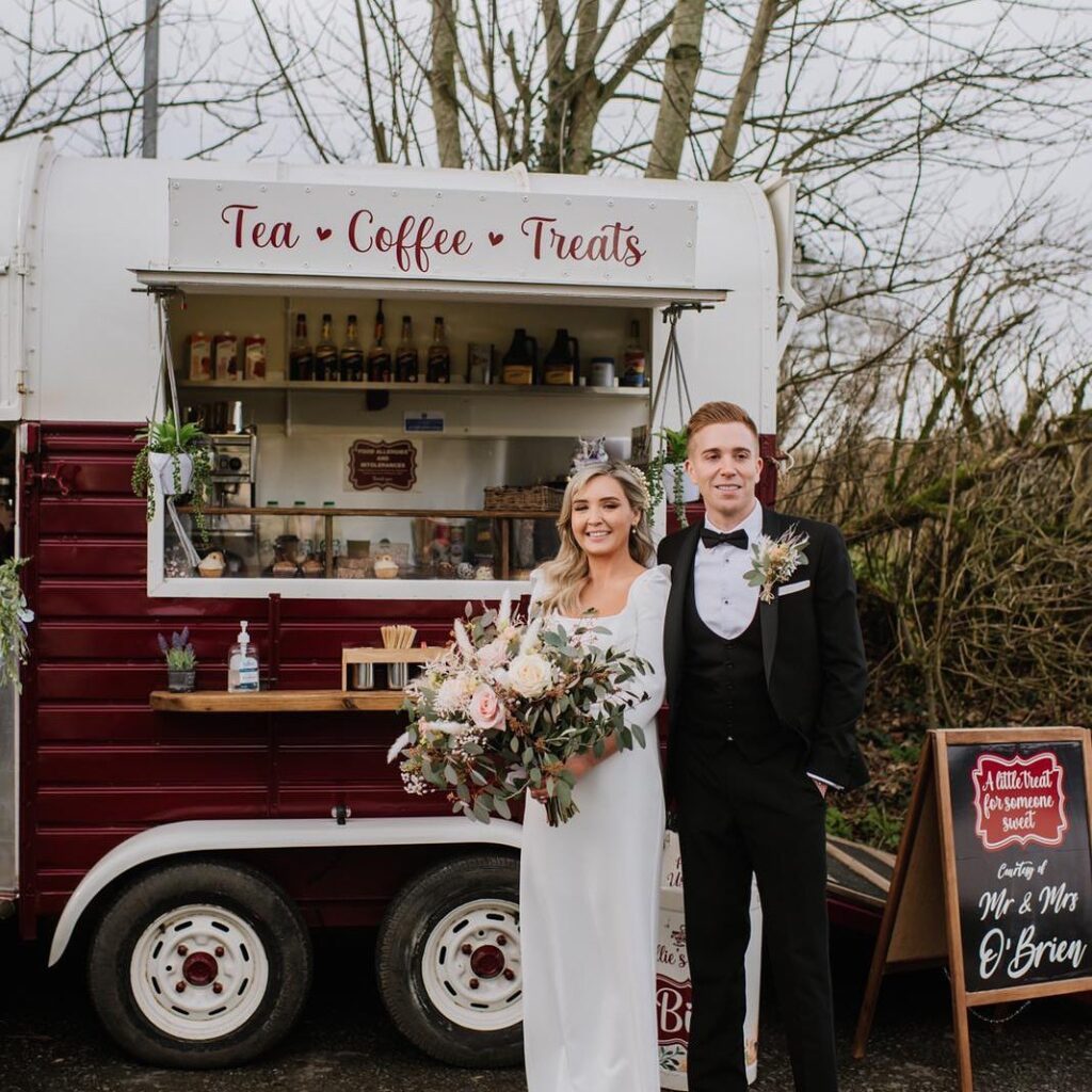 Bride and groom standing by tea and treats trailer with flowers